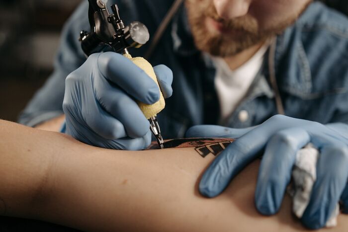 Tattoo artist with gloves applying ink to client's arm with tattoo machine.