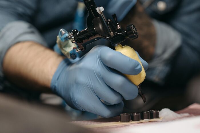 Tattoo artist in blue gloves holding a tattoo machine, preparing for tattoo work.