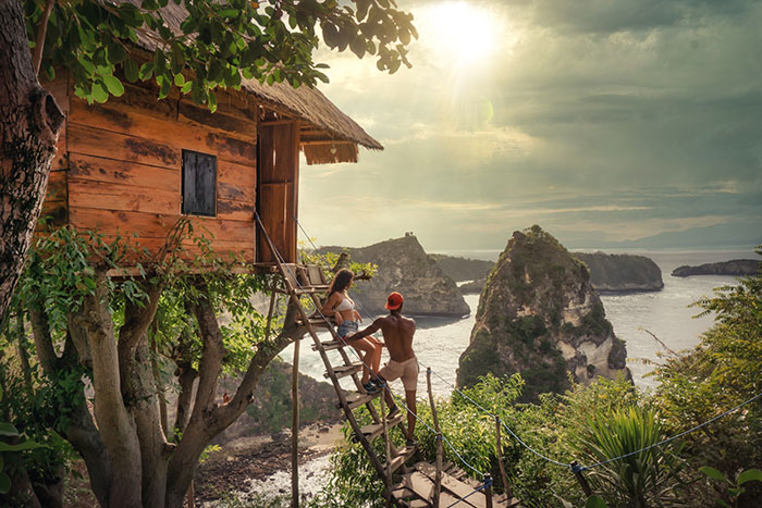 Couple stnading near tree house and looking at sea with rocks
