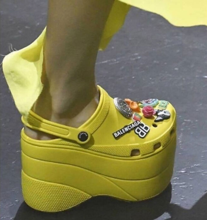 Yellow platform Crocs with Balenciaga logo and colorful charms, showcasing weird shoe design.