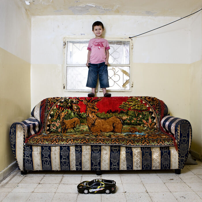 Child standing on colorful sofa with toy car on floor, showcasing children’s toy collections around the world.