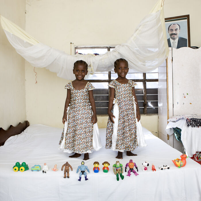 Two girls in matching dresses smiling on a bed displaying toy collections in the Toy Stories series about children worldwide.