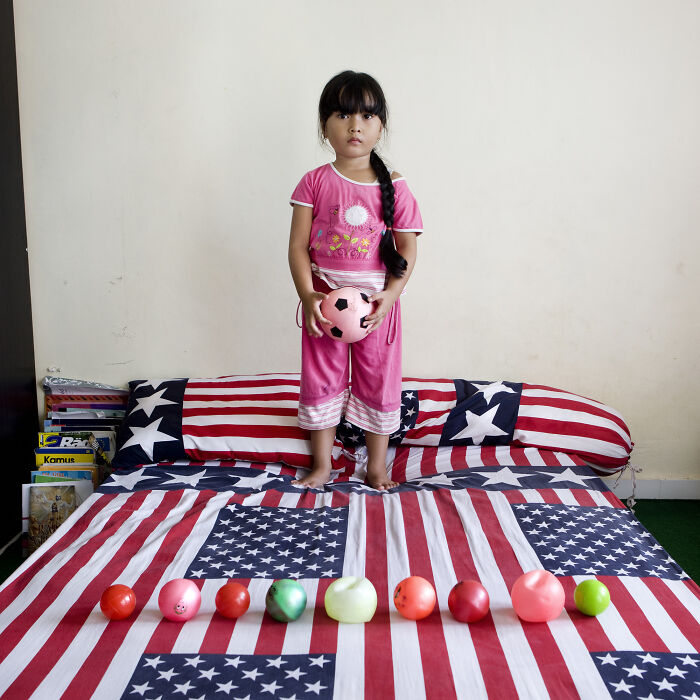Young girl standing on a bed with USA flag bedding holding a pink toy ball, part of a toy stories series showcasing children’s collections.