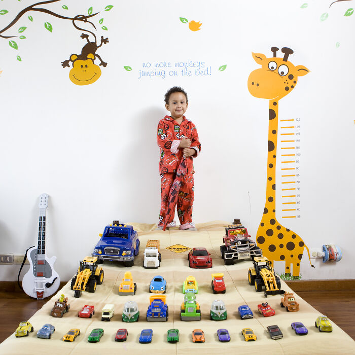 Child in pajamas showcasing toy car collection arranged on a bed, part of the toy collections series featuring children worldwide.