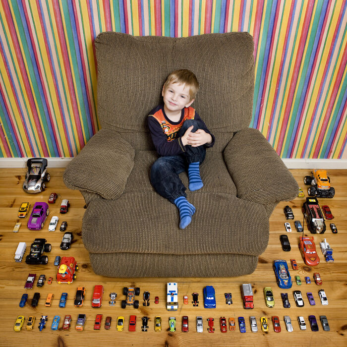Young boy sitting on a large chair surrounded by a diverse toy car collection showcasing children’s toy collections worldwide