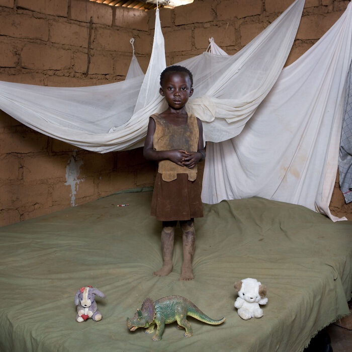 Child in rustic room showcasing toy collection including stuffed animals and a dinosaur, highlighting children around the world.