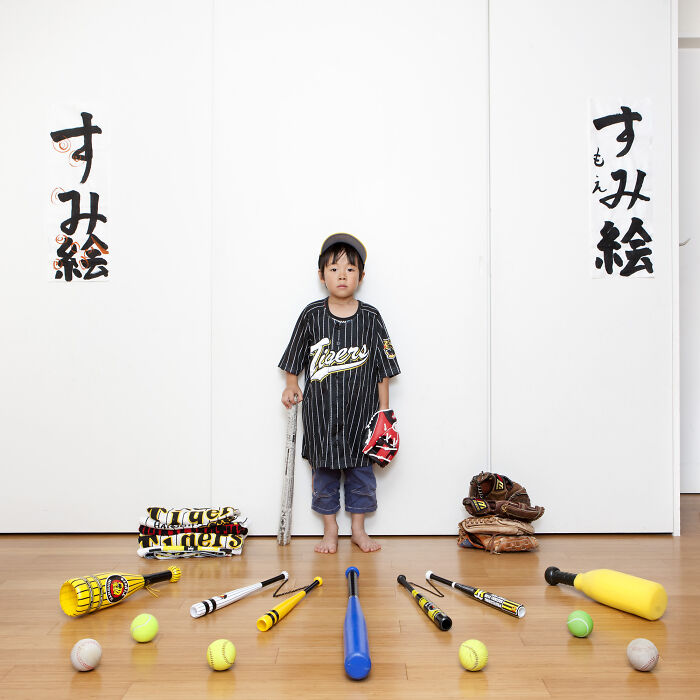 Child from the series Toy Stories posing with baseball bats, balls, gloves, and uniform showcasing toy collections worldwide.