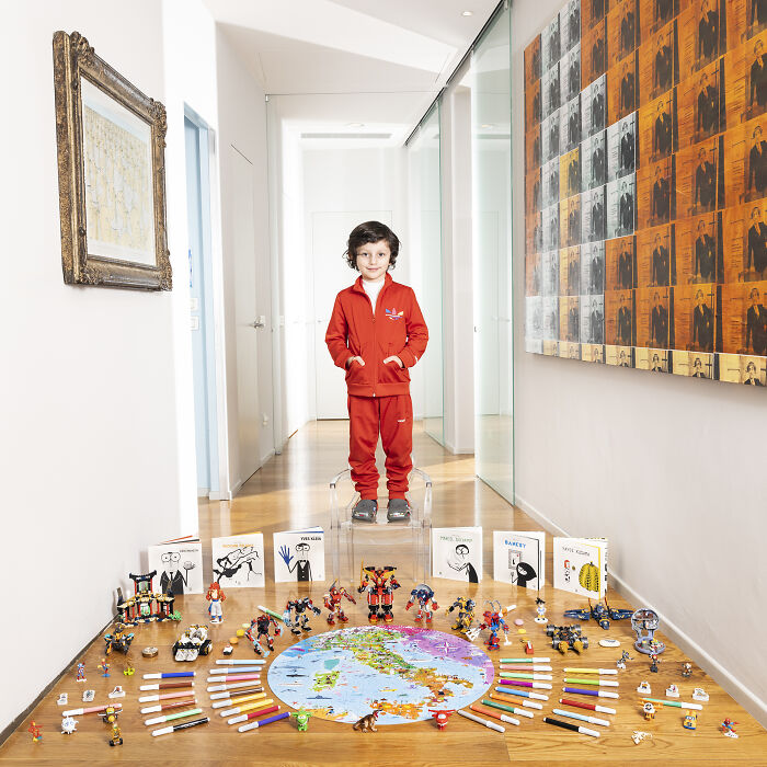 Child standing in a hallway showcasing an extensive toy collection arranged neatly around a world map in a bright, modern home.