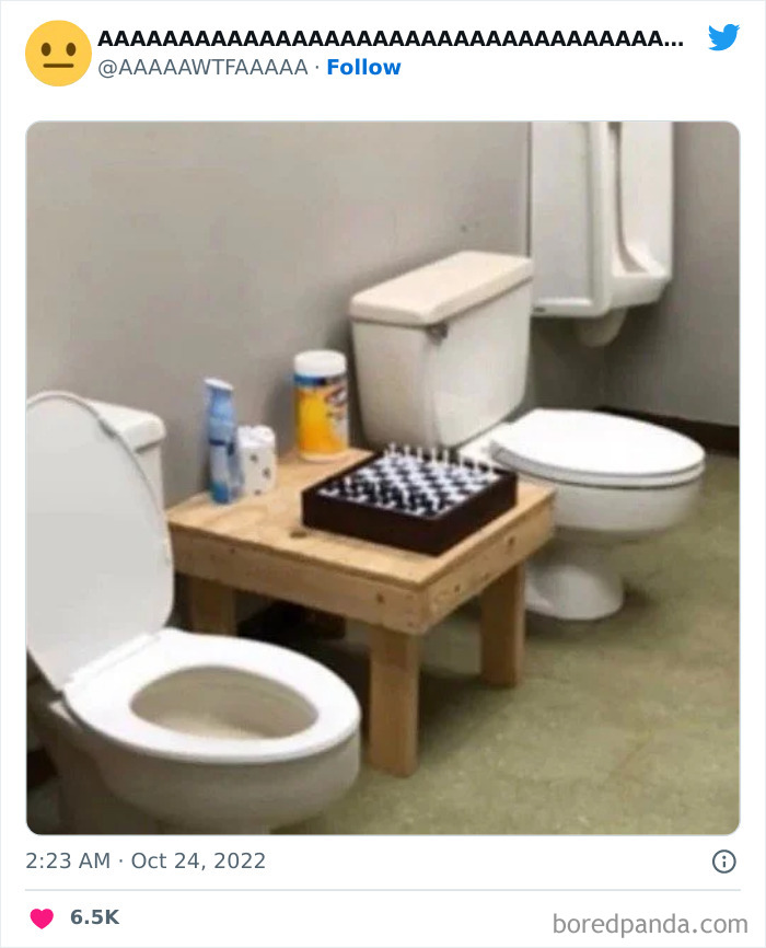 Weird but funny restroom setup with chessboard on a table between two toilets.