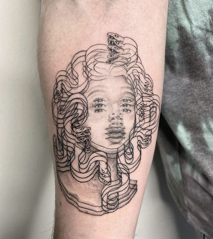 Abstract line tattoo on arm with a face and numerous flowing hair strands; optical illusion effect.
