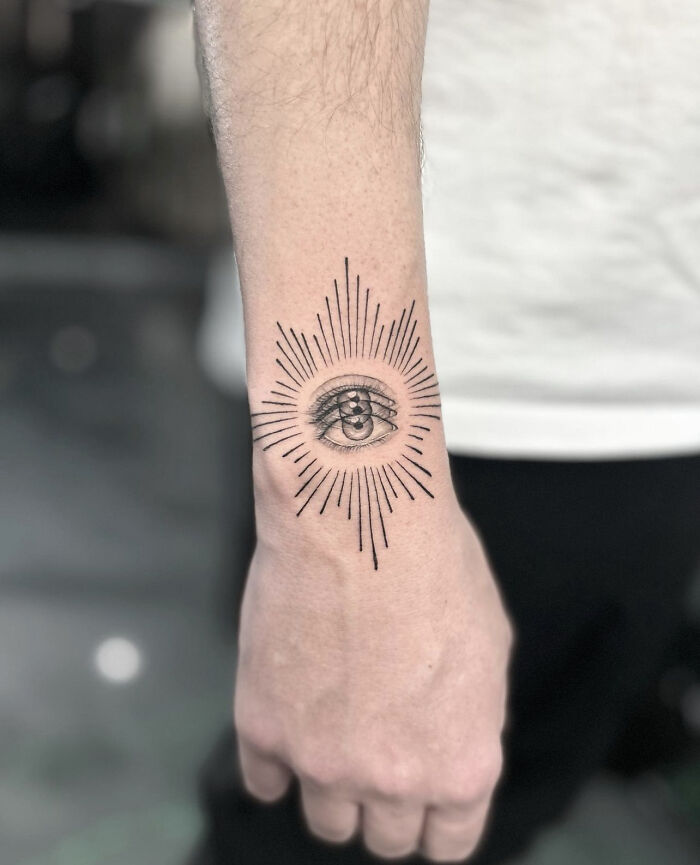 Arm with an eye tattoo featuring radiating lines, creating a dynamic and moving visual effect.