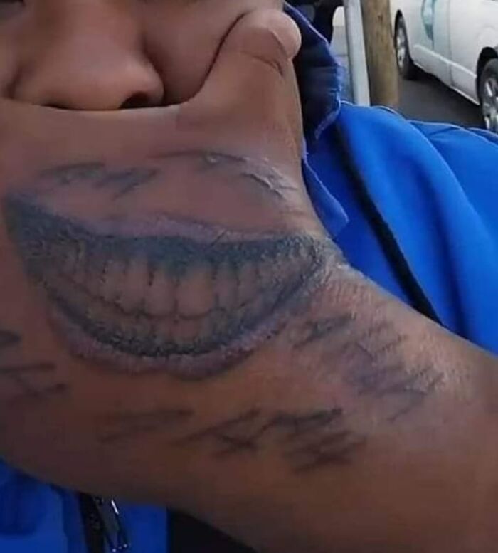 Person covering face with hand displaying a poorly drawn smile tattoo, inkshaming bad tattoos humorously.
