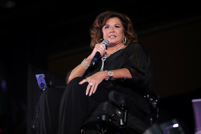 Celebrity speaking on stage, holding a microphone, related to minor and severe crimes.