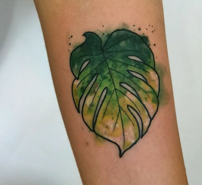 Watercolor tattoo of a Monstera leaf with green and yellow hues on skin.