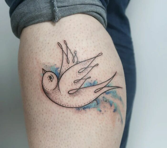 Minimalist bird watercolor tattoo with blue accents on forearm.