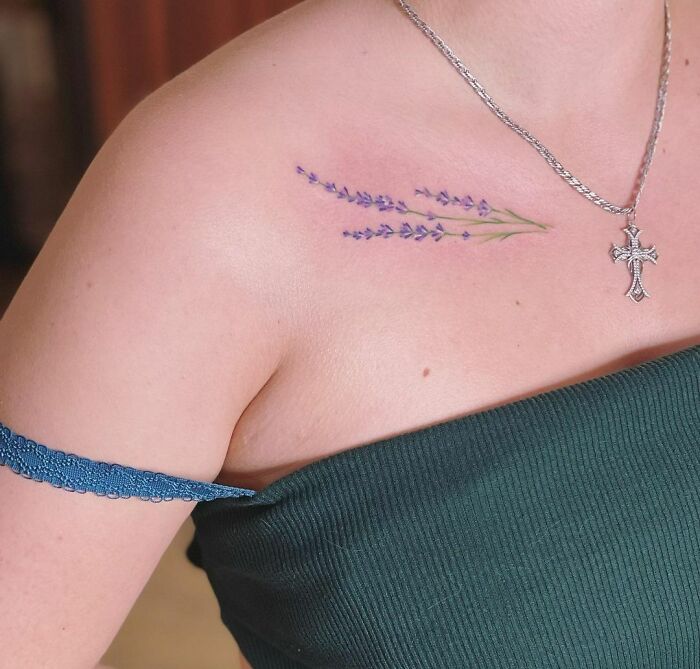 Watercolor tattoo of lavender on shoulder, adorned with a silver necklace and cross pendant.