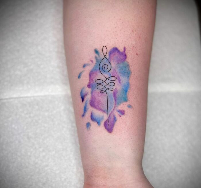 Watercolor tattoo with abstract purple and blue design on forearm.