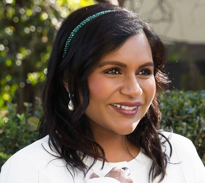 Mindy Kaling smiling outdoors, representing celebrities who never married yet still found love, with a green headband and earrings.