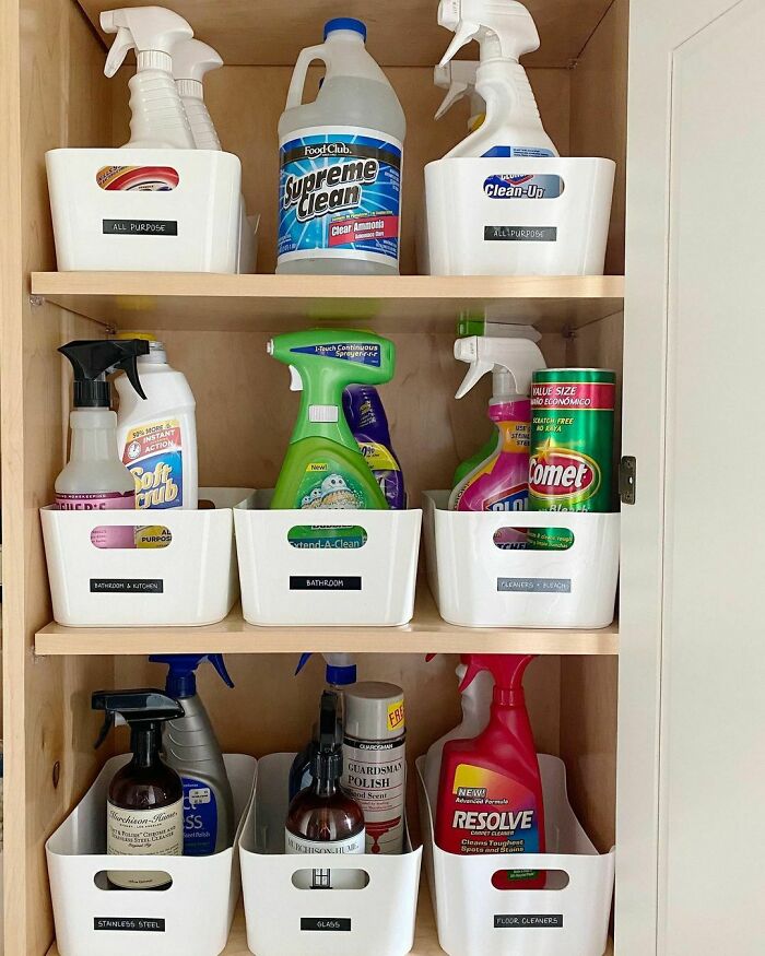 Organized cleaning supplies in labeled bins on wooden shelves for efficient home organization.
