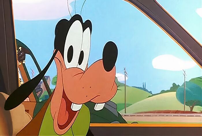Cartoon dog in a car, smiling with an open mouth against a countryside backdrop.