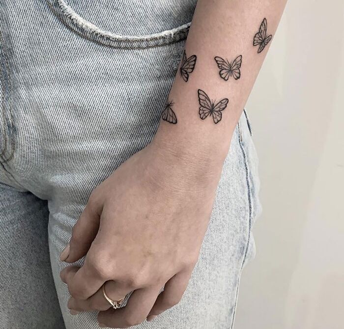 Butterfly animal tattoos on a woman's forearm wearing denim jeans, showcasing creative ink design ideas.