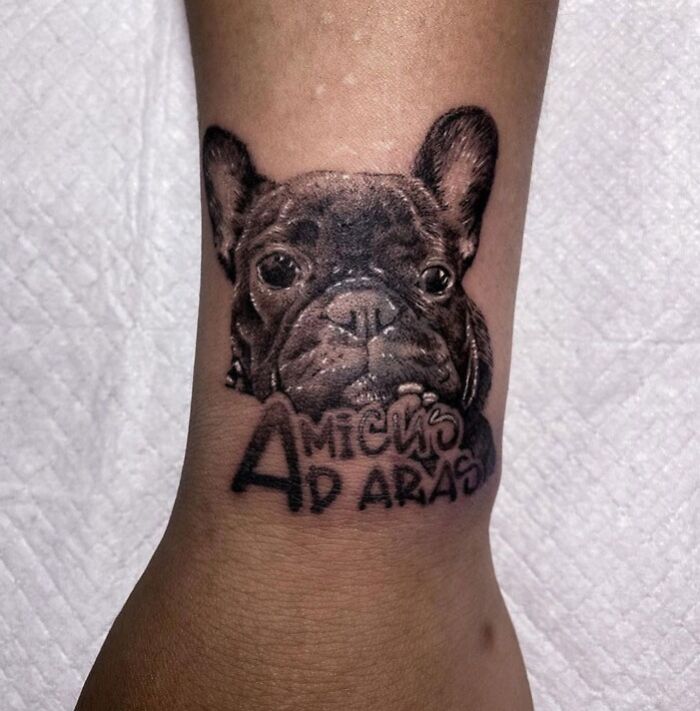 Animal tattoo of a French bulldog with text on a forearm, showcasing detailed design and creativity.