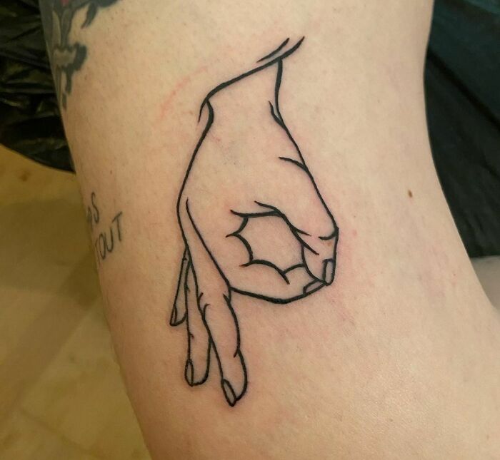 Humorous tattoo of a hand making an OK gesture on skin.