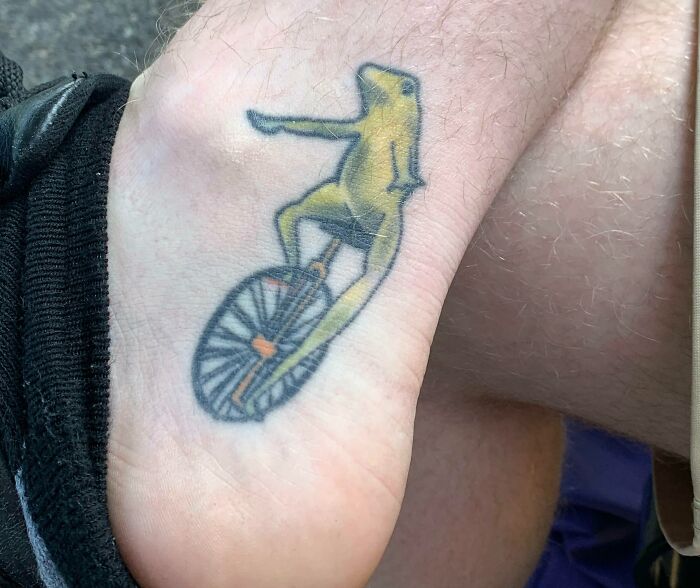 Funny tattoo of a unicycle-riding frog pointing forward.