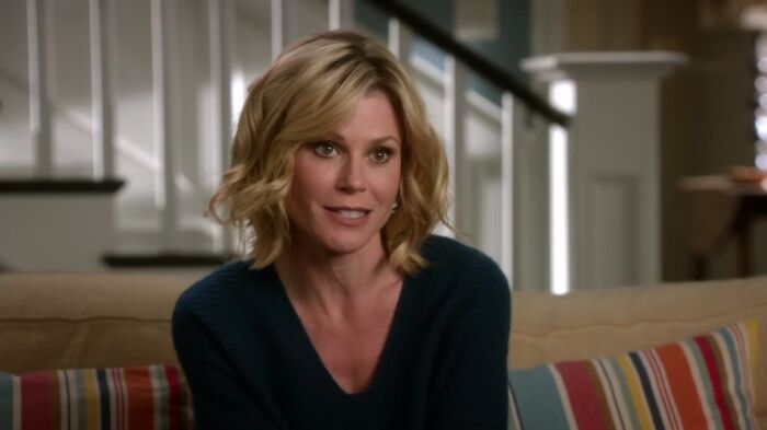 Claire Dunphy, in a dark green sweater, is sitting on the sofa and talking