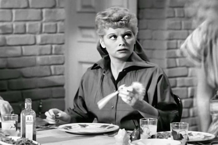 Lucy Ricardo is sitting near the table and is looking suspicious