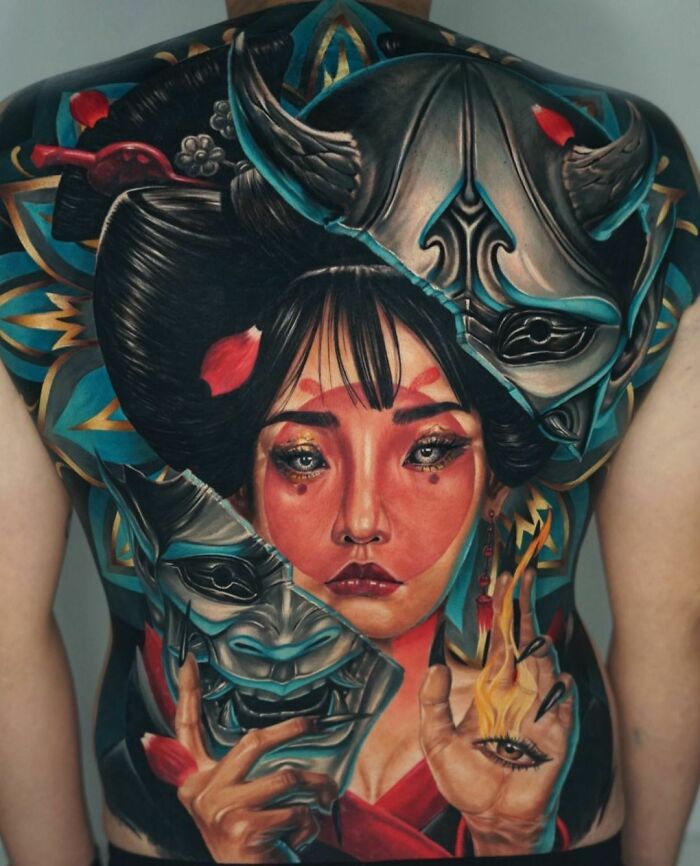 Realistic tattoo of a geisha with a mask and intricate details, covering a person's back.