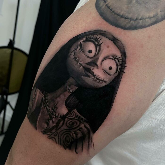 Realistic tattoo of a stitched character with large eyes on an arm, showcasing impressive detail and shading.