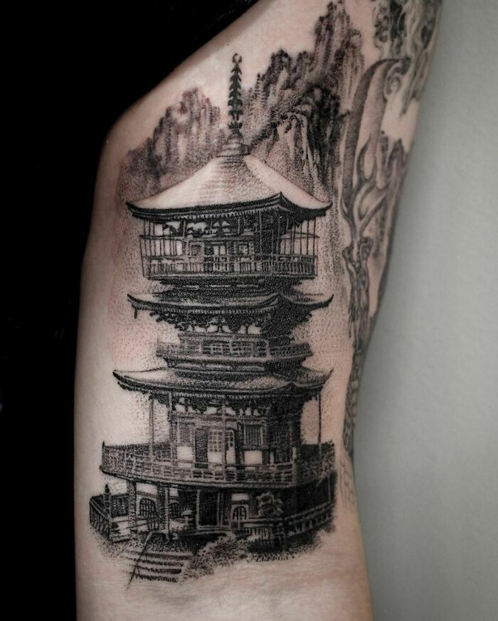 Super realistic tattoo of a detailed pagoda on an arm, showcasing intricate shading and architectural precision.