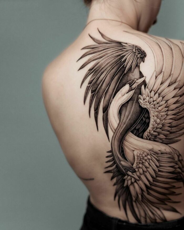 A super realistic tattoo of a detailed, entwined swan and snake covers the person's shoulder and back.