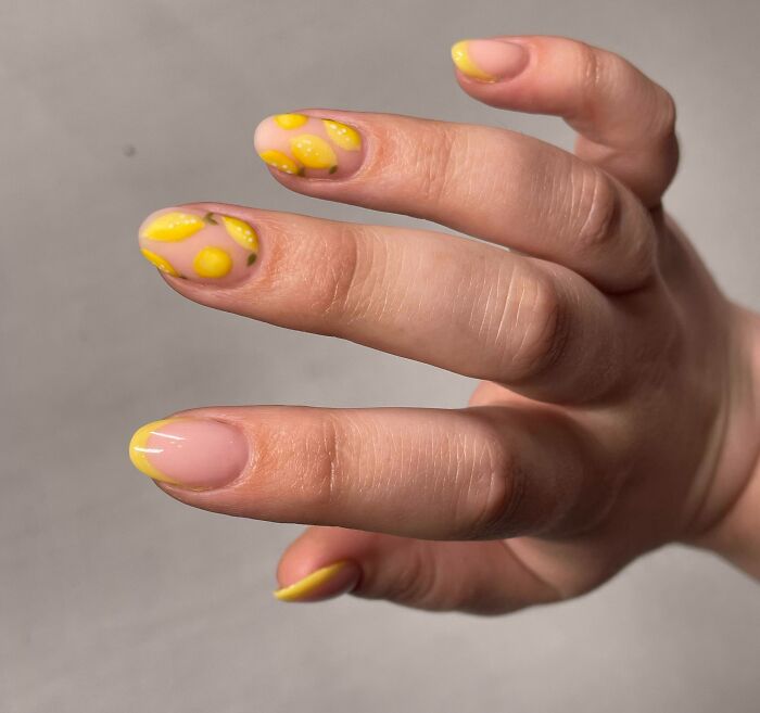Yellow lemon-themed nail art design, featuring intricate patterns on a hand.