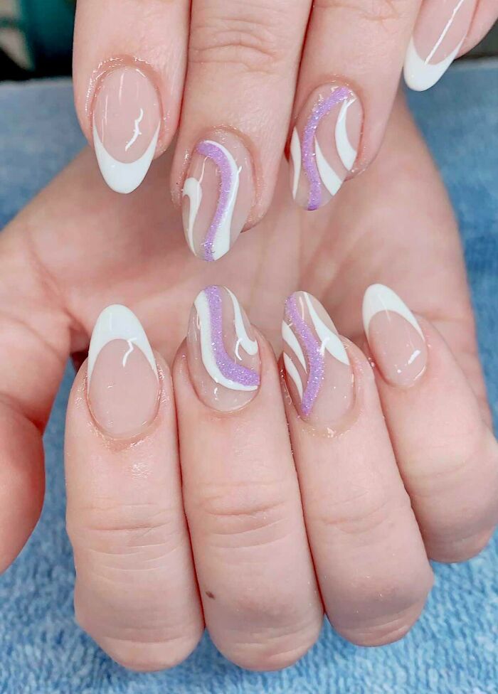 Nail art with white and purple swirls on a n**e base, showcasing creative design ideas for your next appointment.
