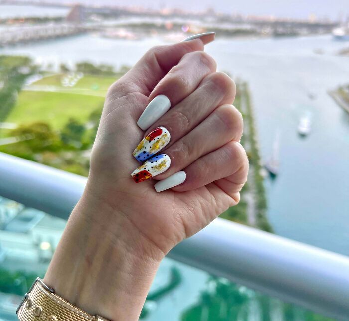 Colorful nail art design with abstract patterns on white nails, overlooking a scenic waterfront view.