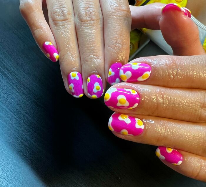 Bright floral nail art with yellow and white daisies on a pink base, showcasing creative nail designs.