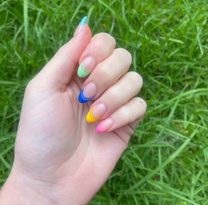 Colorful nail art design with pastel and bright hues on a background of green grass.