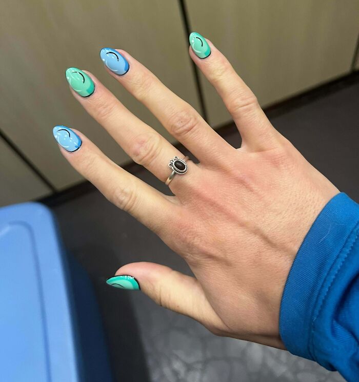 Colorful nail art with blue and green swirls, adorned with a black stone ring.