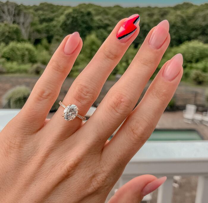Close-up of a hand showcasing nail art with a pink design, wearing a sparkling diamond ring.