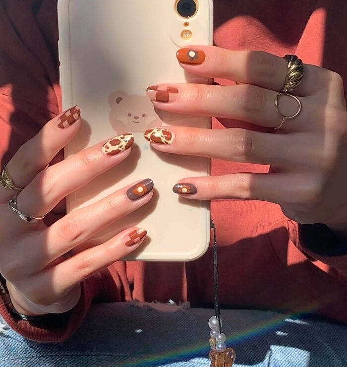 Unique nail art ideas featuring giraffe patterns and plaid designs, holding a phone with cute bear case.