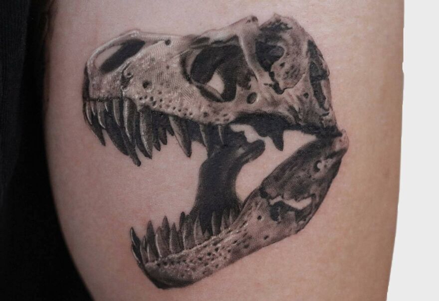 Realistic tattoo of a dinosaur skull, detailed and lifelike, showcasing artistic skill on skin.