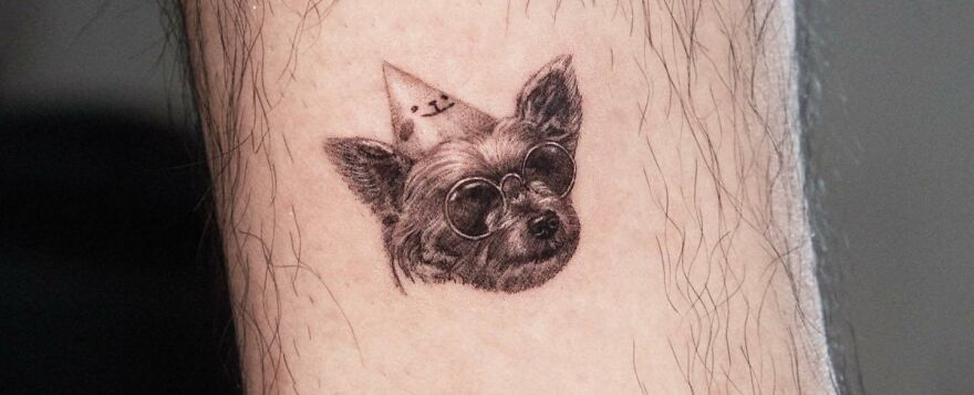 Realistic tattoo of a dog wearing sunglasses and a party hat on human skin.