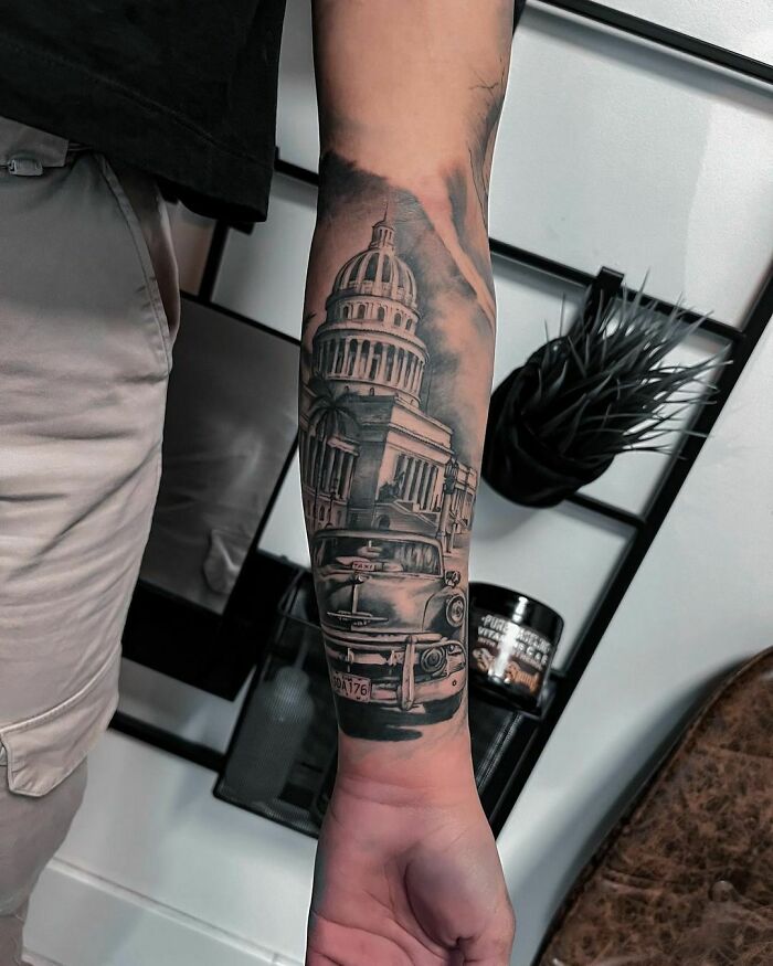 Realistic tattoo of a vintage car and a building on a forearm, showcasing intricate detail and artistic skill.