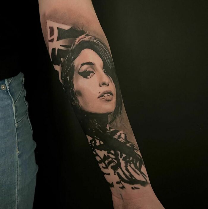 Realistic tattoo of a woman's face on an arm, showcasing intricate artistry against a black background.