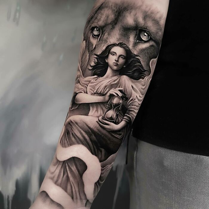 Realistic tattoo featuring a woman holding an hourglass, surrounded by a lion's eyes, inked on an arm.
