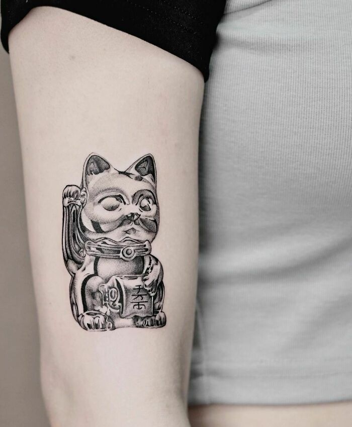 Super realistic tattoo of a Japanese lucky cat on a person's arm, featuring intricate shading and detail.