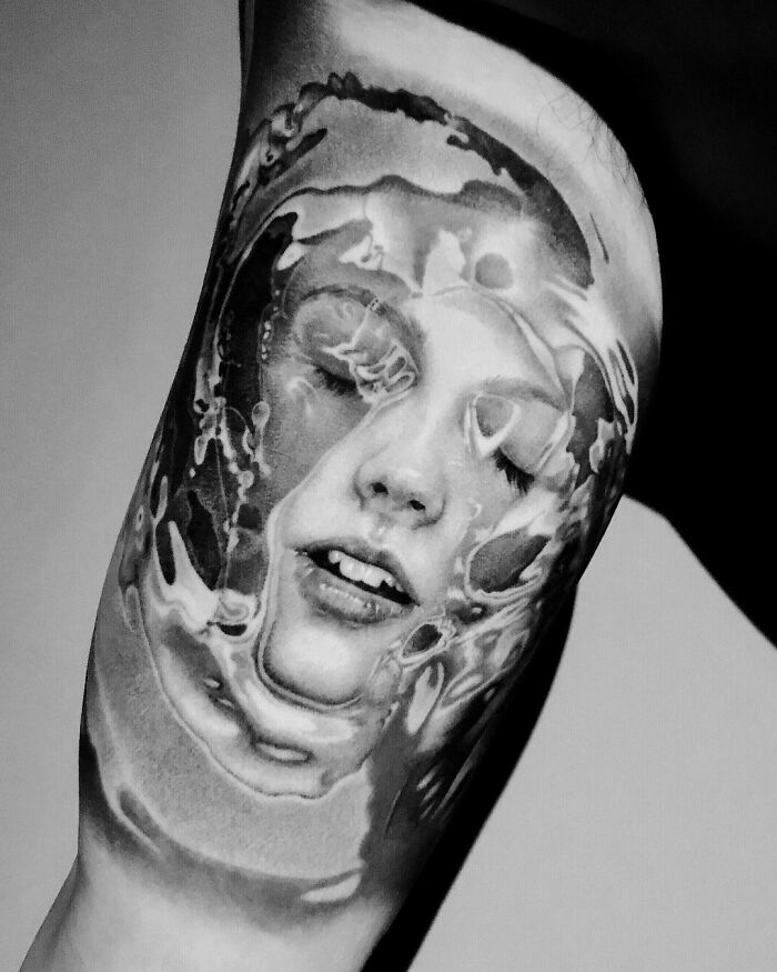 Super realistic tattoo of a woman's face submerged in water on a forearm, showcasing fine details and shading.