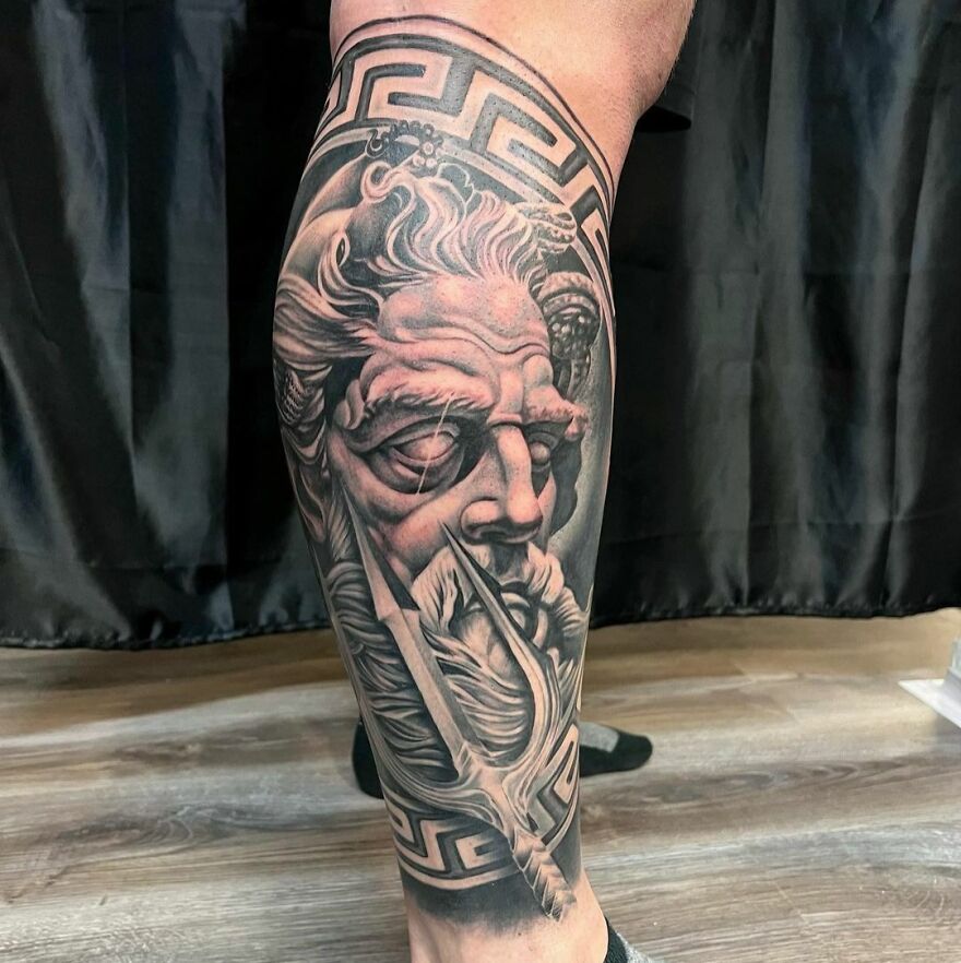 Realistic tattoo of a Greek god's face with intricate details on a person's leg.